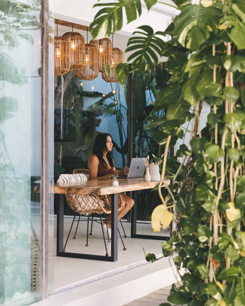A girl working on her laptop in a coworking space with transparent glass sliders and leaves around.