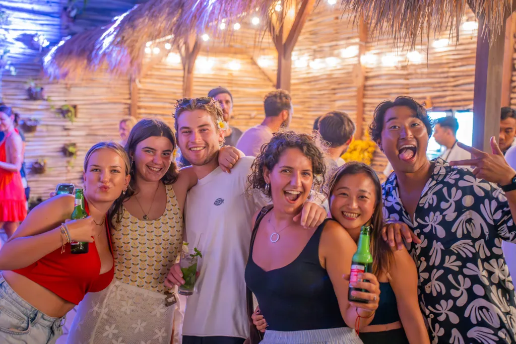 6 happy guests holding beers and smiling at the camera at a party.