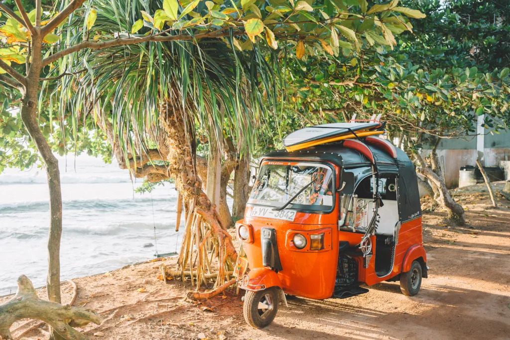 A tuk tuk parked at the beach with two surfboards on the roof