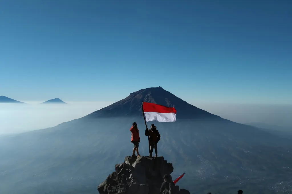 Two people standing on a rock with Mount agung in the back, holding the Indonesian flag