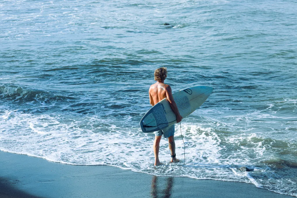 A man walking into the ocean holding a surfboard