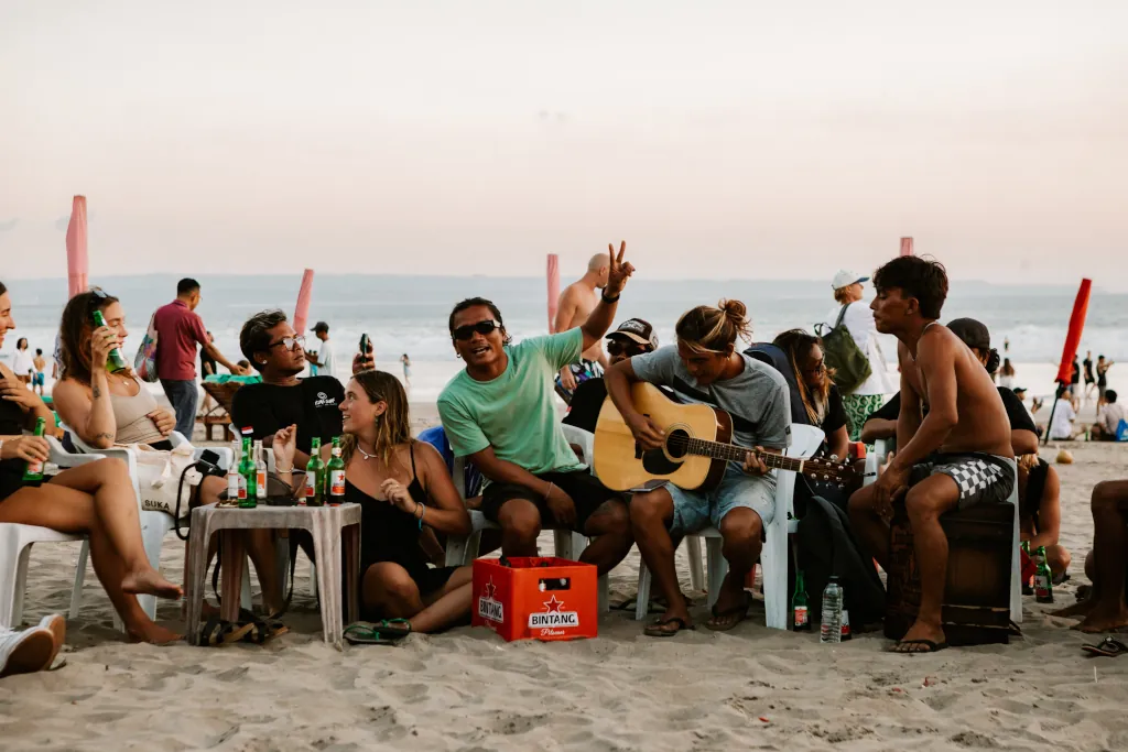 Guests and surf guides sitting together on a beach during sunset, singing and drinking beers.