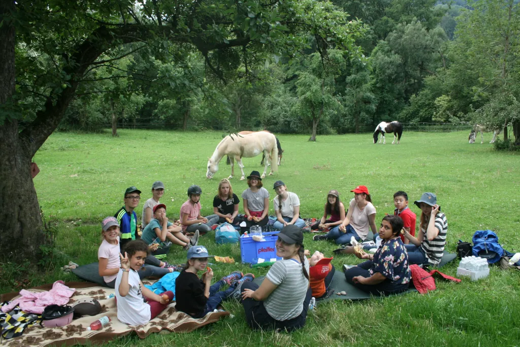 A group of kids in a park having a picnic with horses in the background
