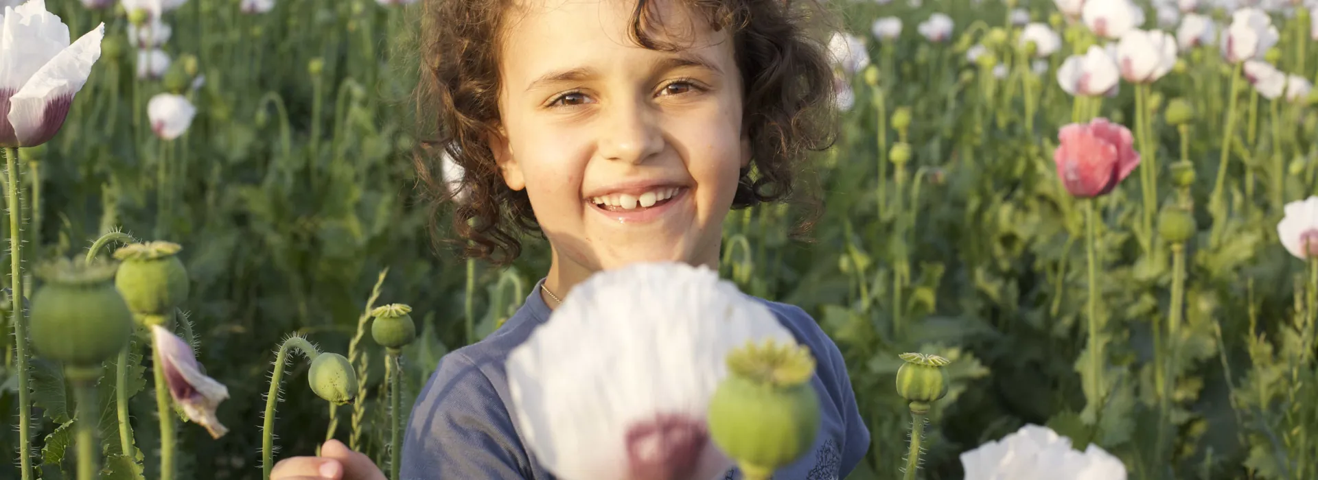 A YOUNG GIRL SMILING AT THE CAMERA HOLDING A FLOWER IN A FIELD OF FLOWERS