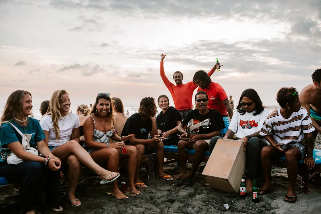 Guests and locals on a beach sitting on sunbeds with guitars and drums, jamming to the sunset.