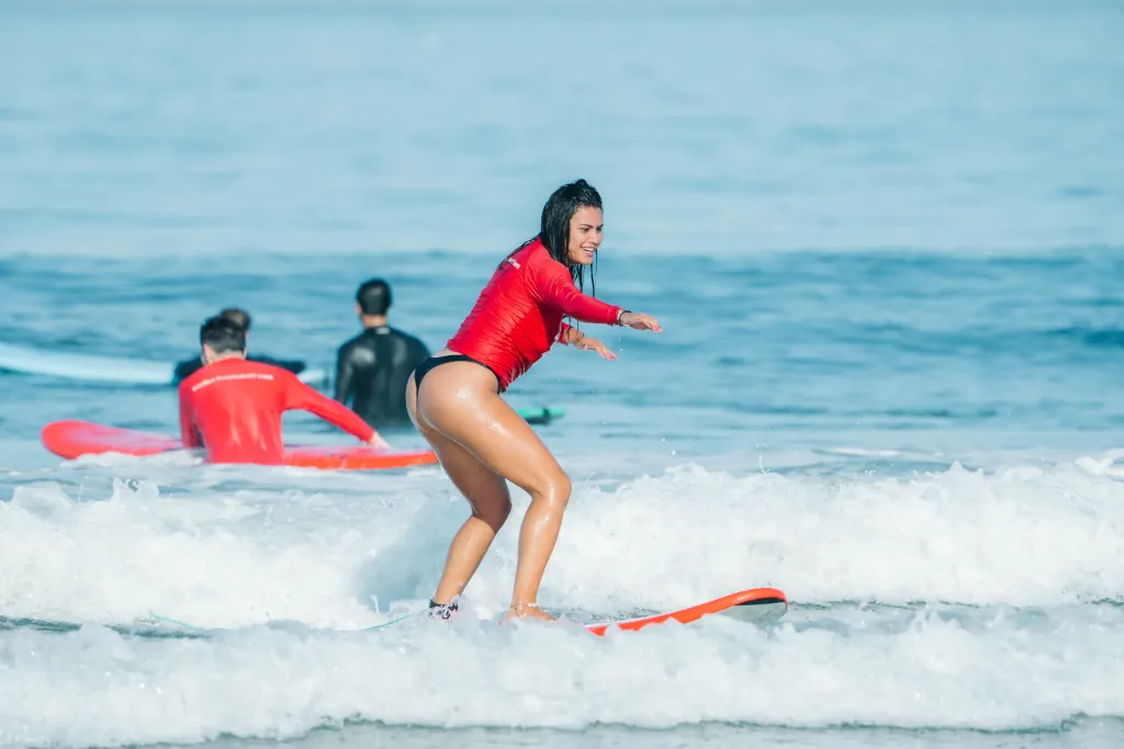 a girl standing and surfing on a red foam top surfboard