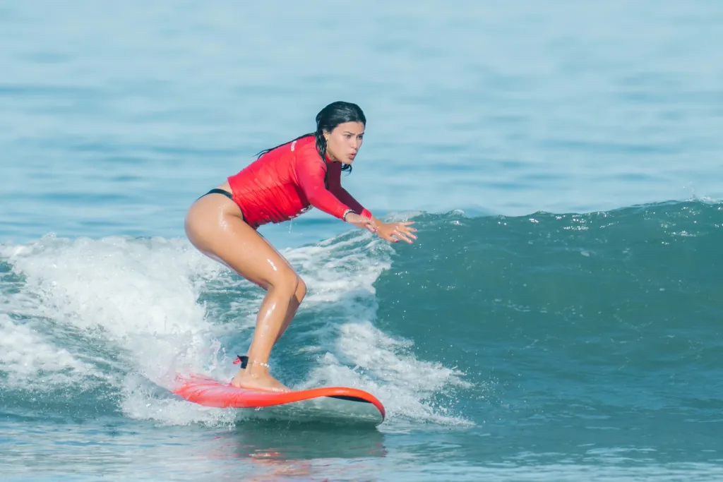 a girl standing on a red soft top learning to surf