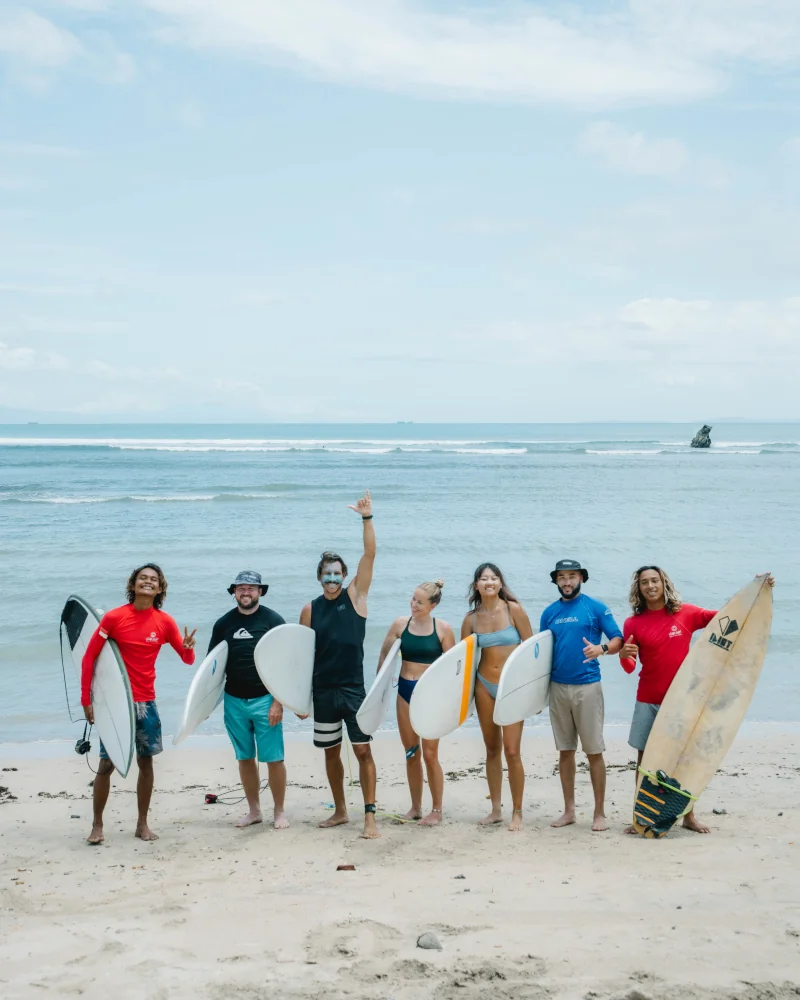 Happy surfers standing on the beach with their surf guides and surfboards smiling