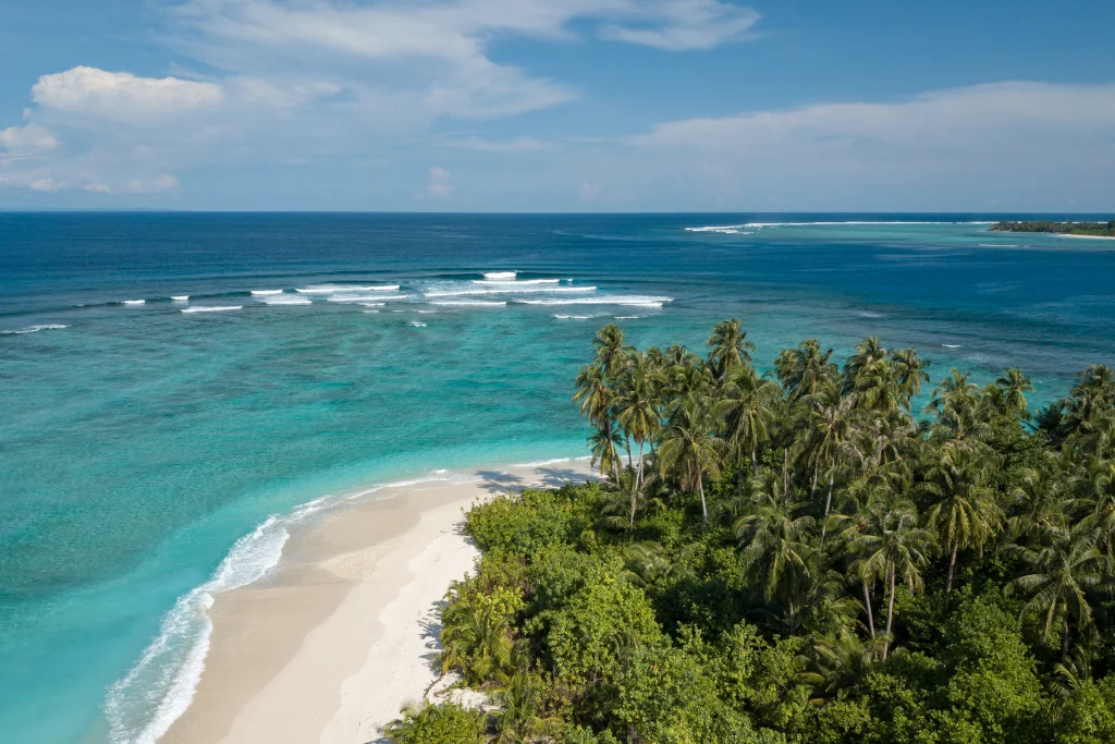 A drone image of the mentawais, white-sand beaches, blue water, waves and palm trees
