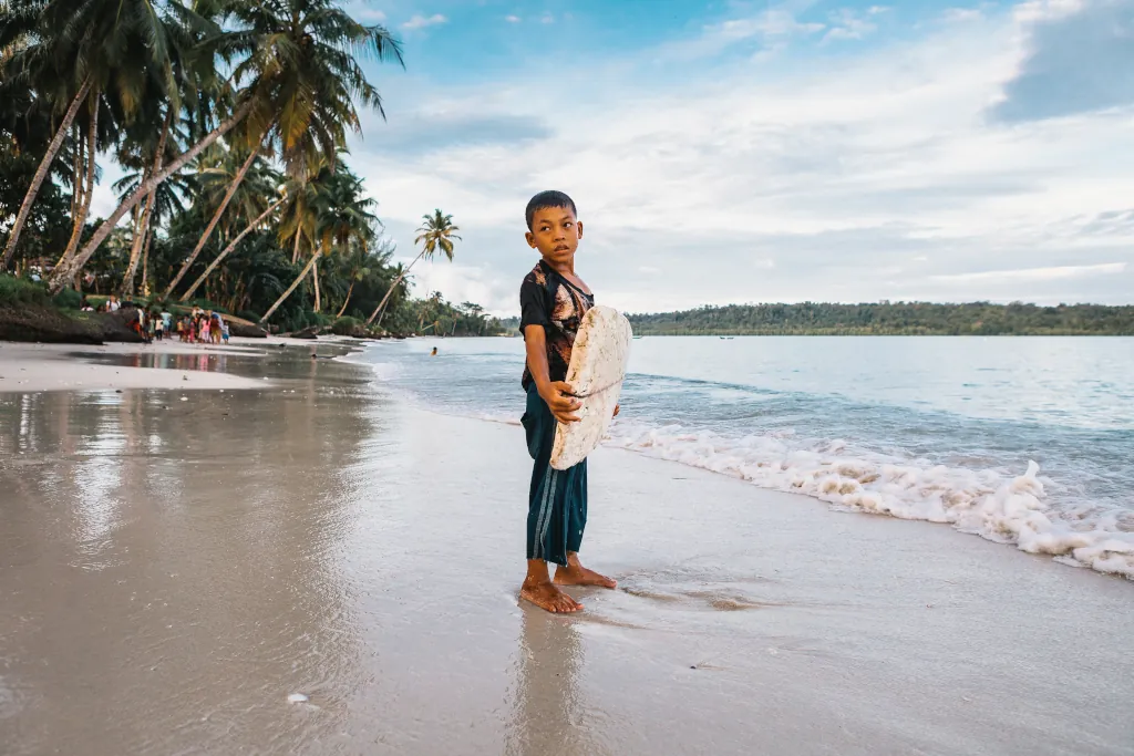 A local boy holding a surfboard on the beach front