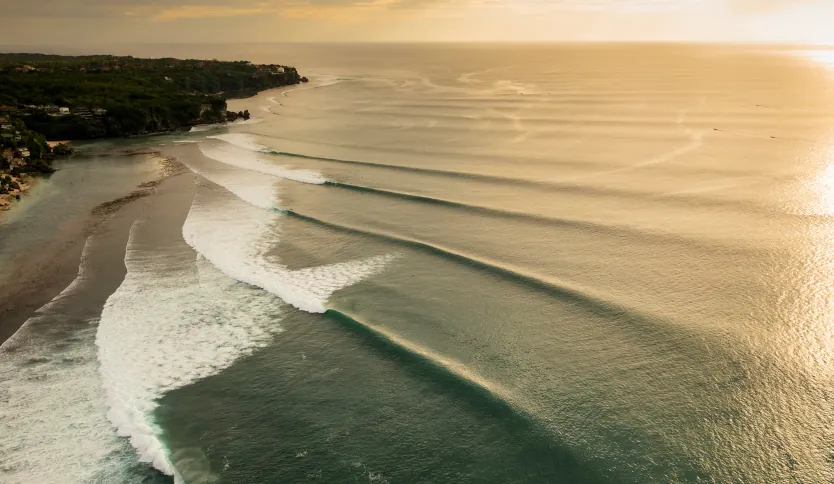 Multiple clean, rolling waves breaking at Uluwatu Beach in Bali under a clear blue sky, ideal for surfing.
