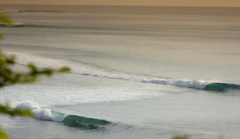 Gentle waves rolling along Uluwatu Beach at sunrise or sunset, with golden light reflecting on the wate.