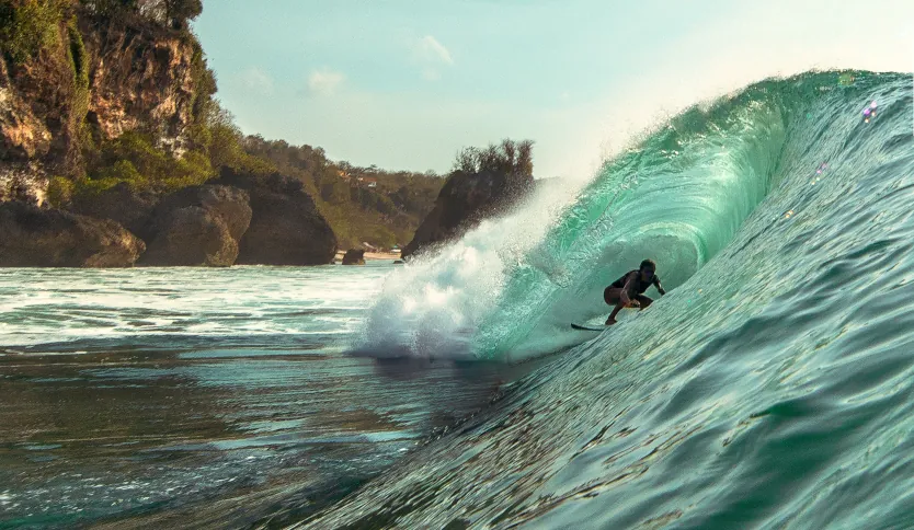 Surfer riding barrel at Impossible Beach in Uluwatu in front of the towering cliffside.