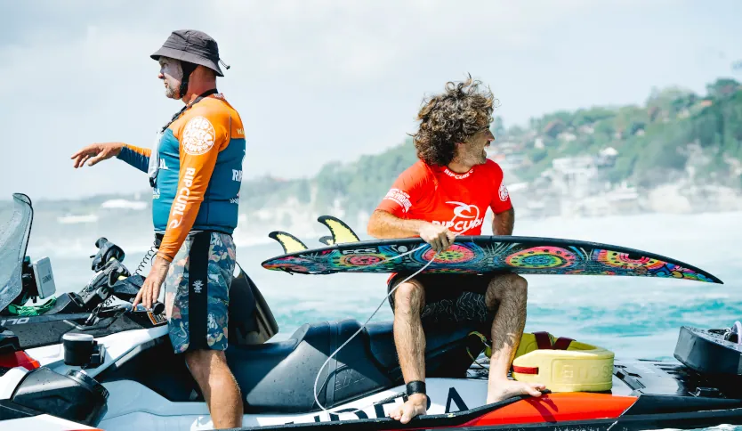 A professional surfer holding his surfboard sitting on a jetski in the ocean.