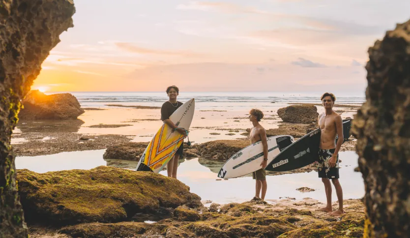 Sinar Tandjung, Bronson Meydi and Varun Tandjung holding their surfboards and standing amongst the rock pools watching the sunset.