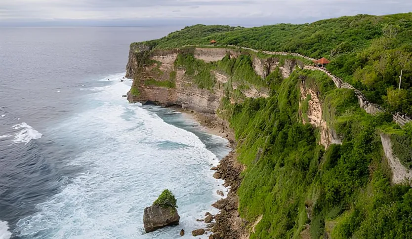 View of Uluwatu's shoreline featuring greenery, rocks, and crashing waves.