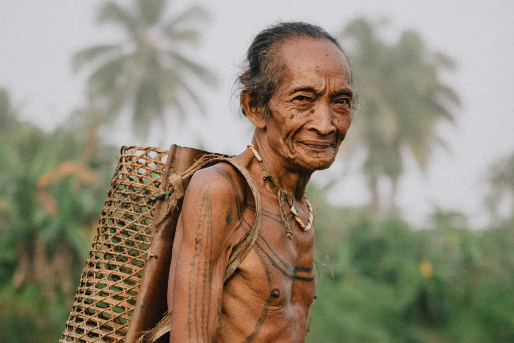 A man from the mentawai tribe with a woven basket on his back, smiling at the camera.