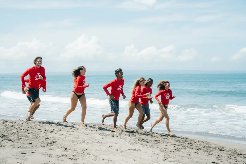 students and surf guides from Kima Surf School running on the beach in a line, with red lycras on.
