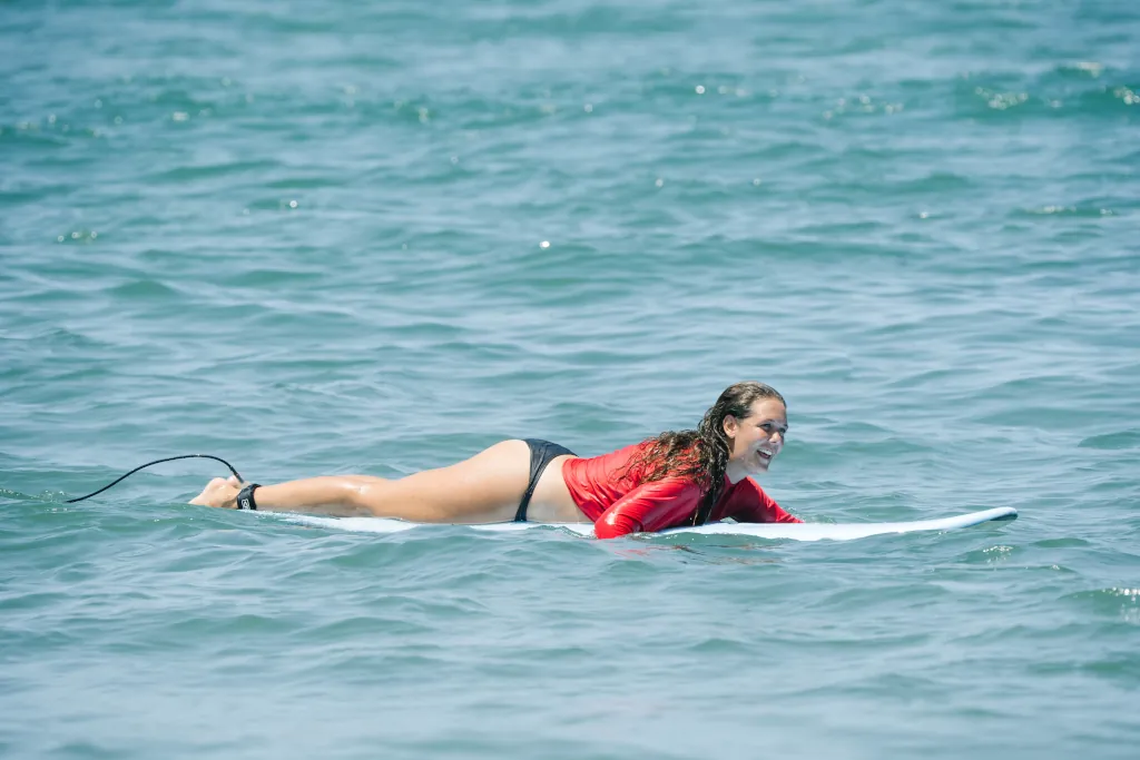 a surfer paddling on a blue soft top foam board wearing a red lycra.