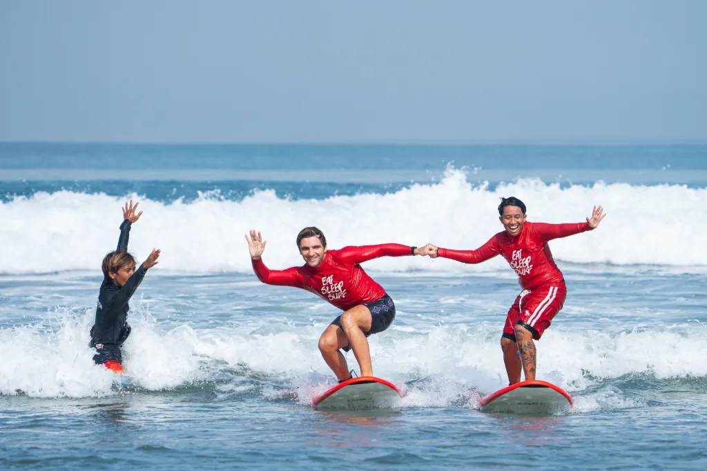 A surfer and the surf guide catching a wave together and holding hands